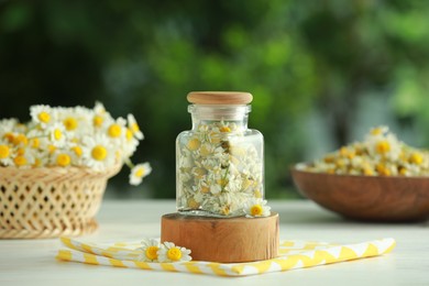 Photo of Dry and fresh chamomile flowers in glass jar on light table against blurred green background