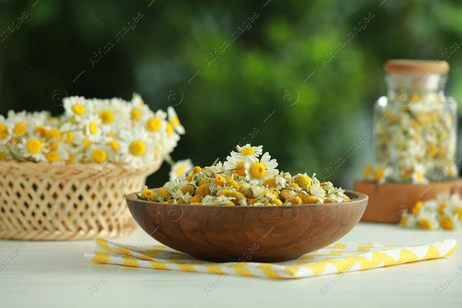 Photo of Dry and fresh chamomile flowers in bowl on light table against blurred green background