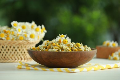 Dry and fresh chamomile flowers in bowl on light table against blurred green background