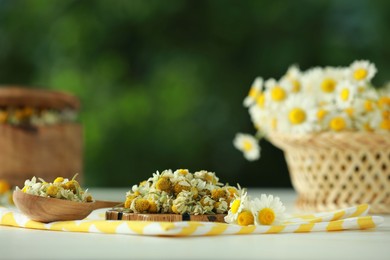 Photo of Dry and fresh chamomile flowers on light table against blurred green background