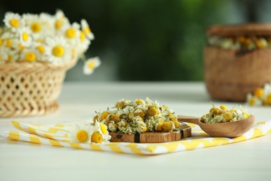 Photo of Dry and fresh chamomile flowers on light table against blurred green background