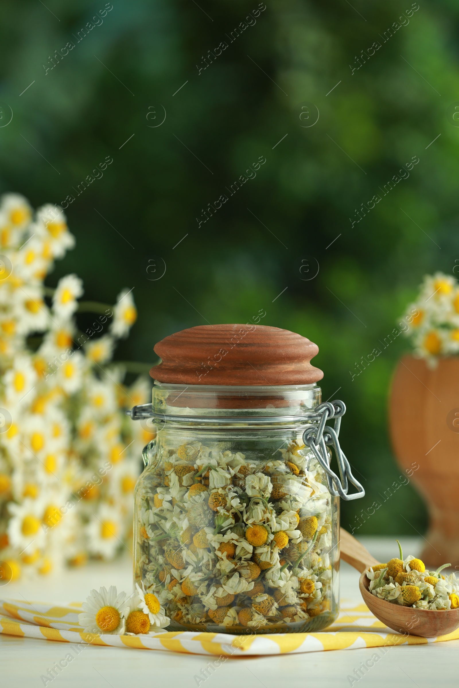 Photo of Dry and fresh chamomile flowers on light table against blurred green background