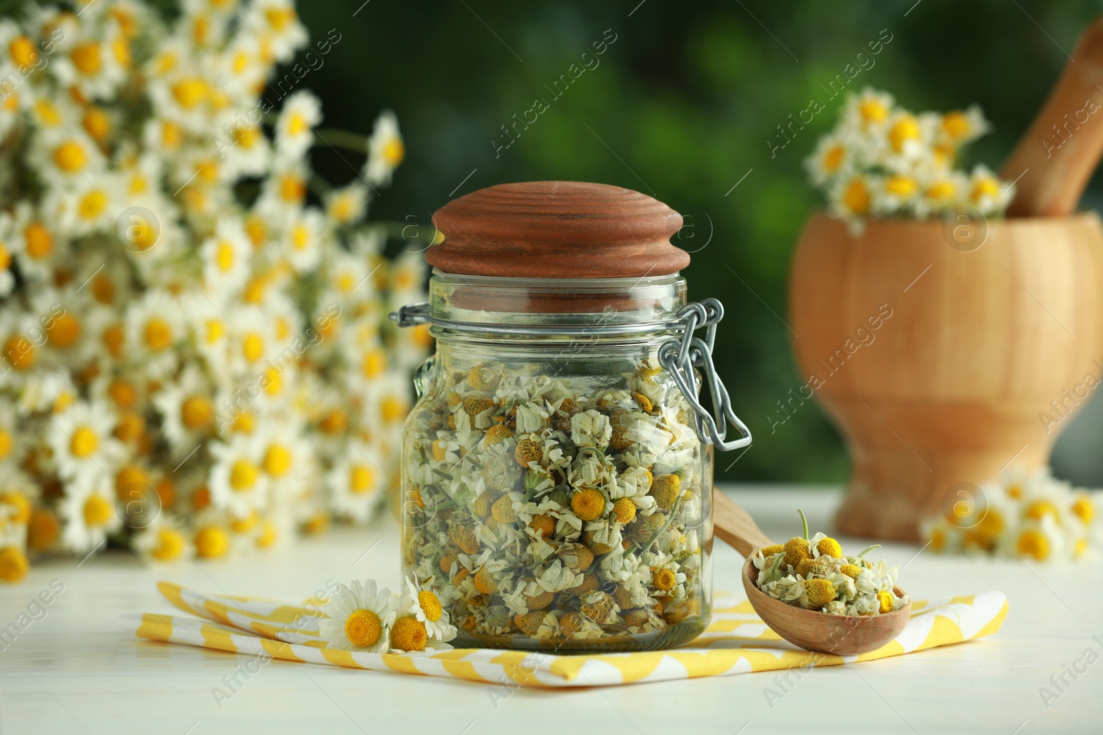 Photo of Dry and fresh chamomile flowers on light table against blurred green background