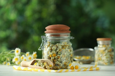 Dry and fresh chamomile flowers on light table against blurred green background