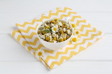 Photo of Dry and fresh chamomile flowers in bowl on white wooden table