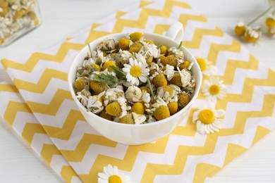 Photo of Dry and fresh chamomile flowers in bowl on white wooden table