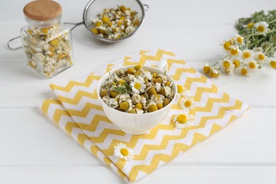 Photo of Dry and fresh chamomile flowers in dishware on white wooden table