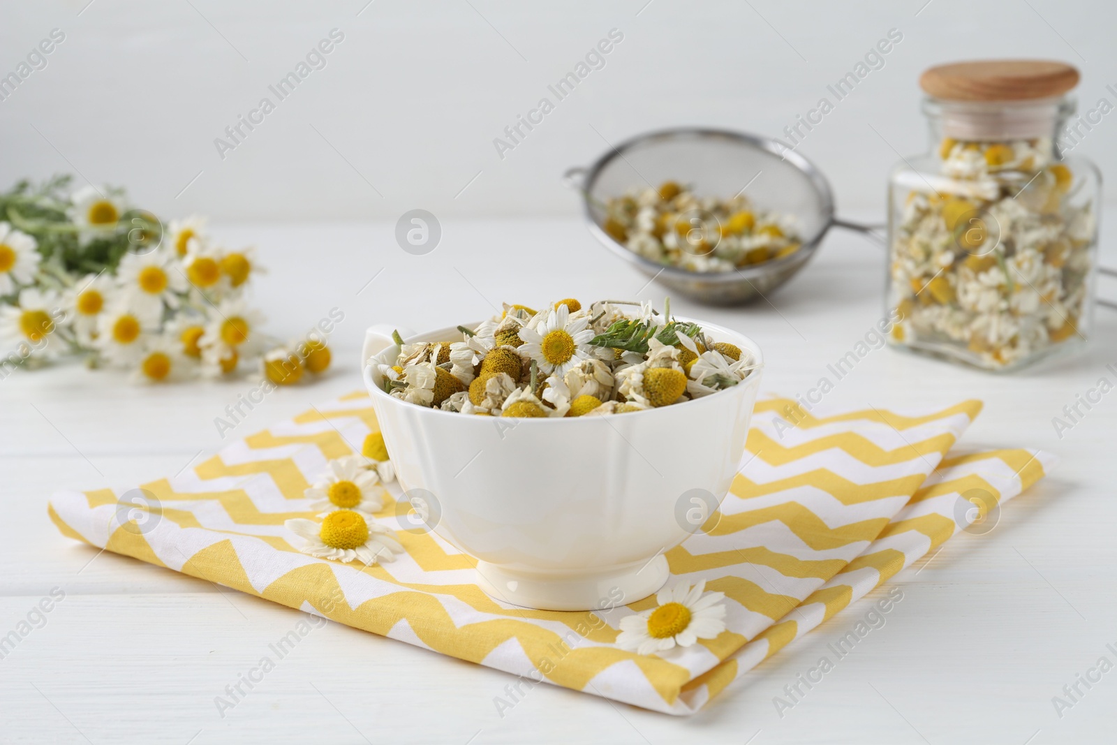 Photo of Dry and fresh chamomile flowers in bowl on white wooden table