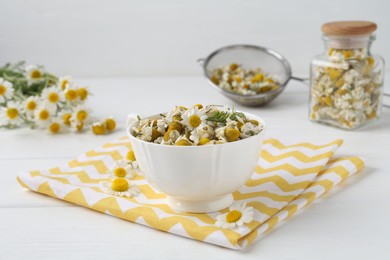 Dry and fresh chamomile flowers in bowl on white wooden table