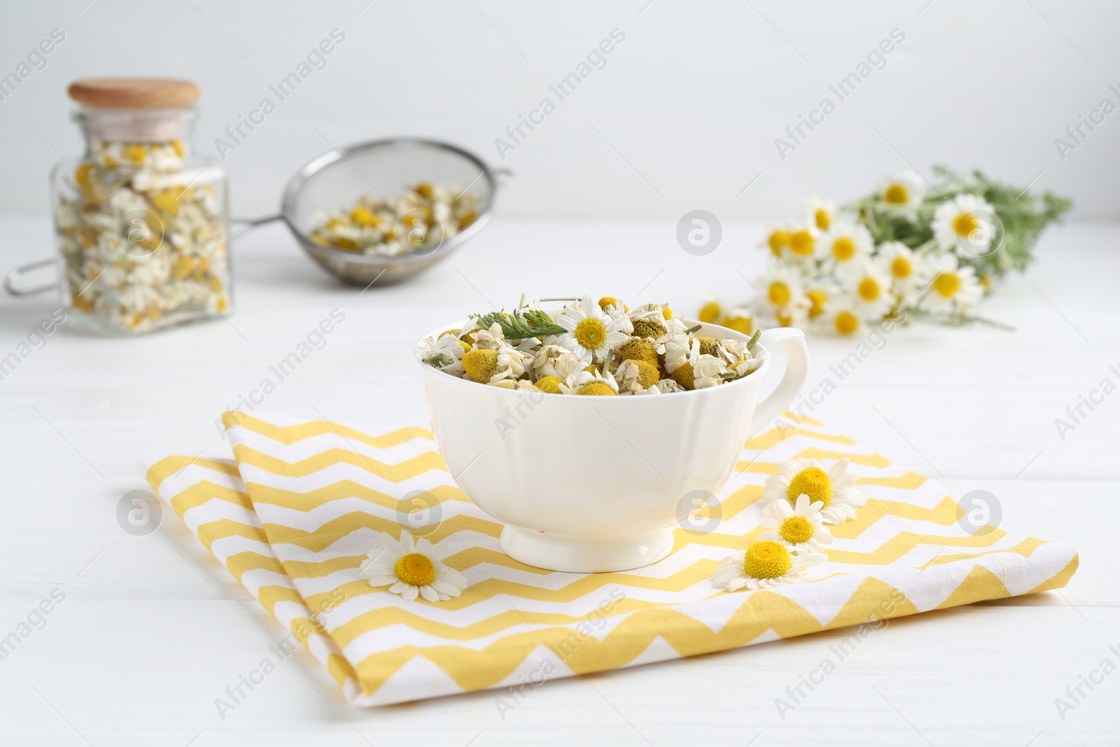 Photo of Dry and fresh chamomile flowers in bowl on white wooden table