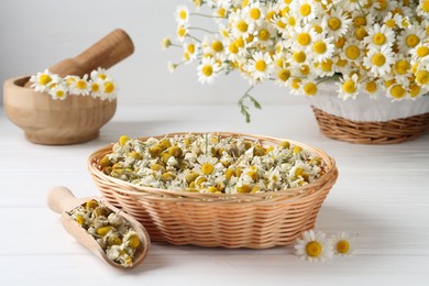 Photo of Dry and fresh chamomile flowers on white wooden table