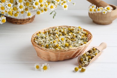 Photo of Dry and fresh chamomile flowers on white wooden table