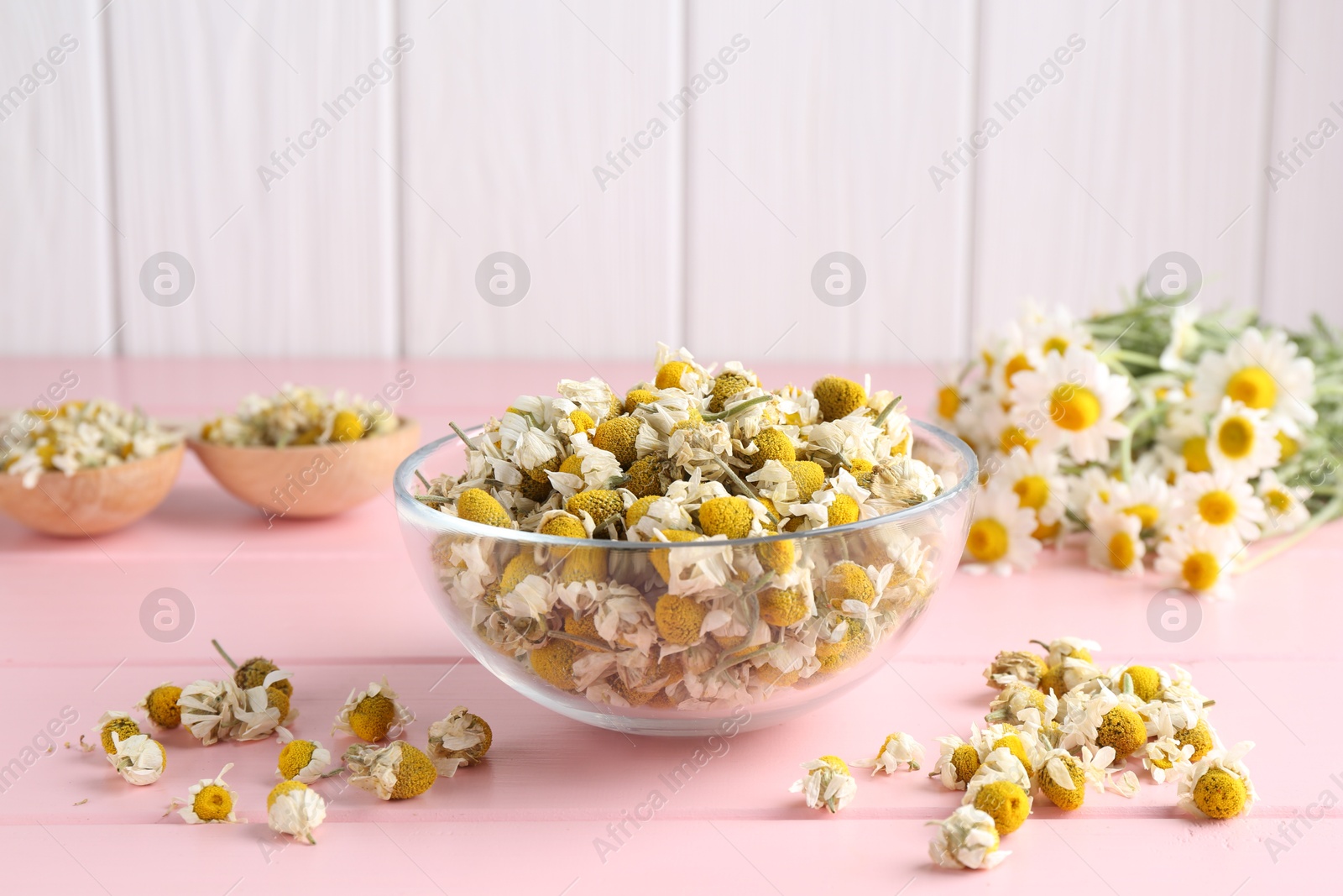 Photo of Chamomile flowers in glass bowl on pink wooden table