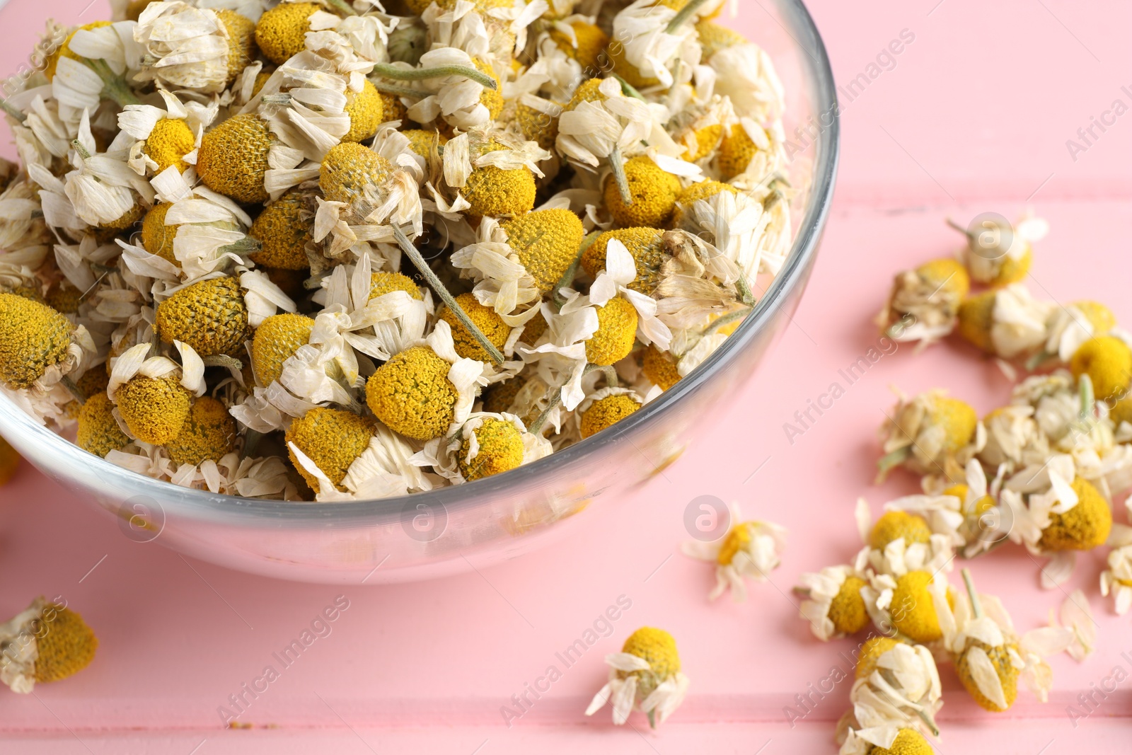 Photo of Chamomile flowers in glass bowl on pink wooden table, closeup