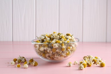 Photo of Chamomile flowers in glass bowl on pink wooden table