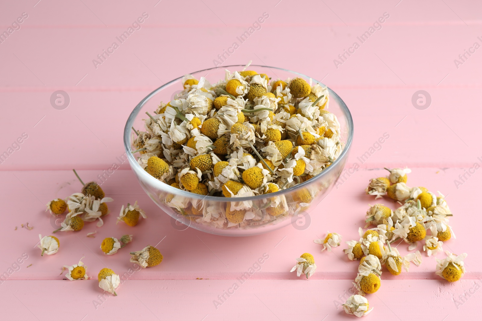 Photo of Chamomile flowers in glass bowl on pink wooden table