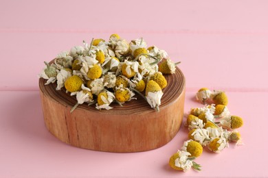 Photo of Chamomile flowers and stump on pink wooden table, closeup