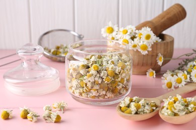 Dry and fresh chamomile flowers in dishware on pink wooden table