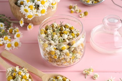 Photo of Dry and fresh chamomile flowers in dishware on pink wooden table, closeup