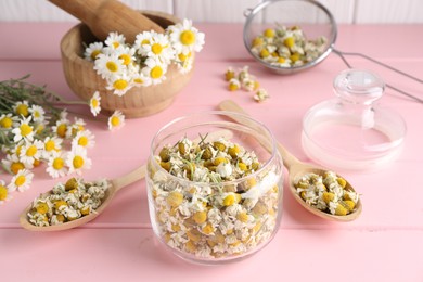 Dry and fresh chamomile flowers in dishware on pink wooden table