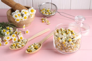 Photo of Dry and fresh chamomile flowers in dishware on pink wooden table