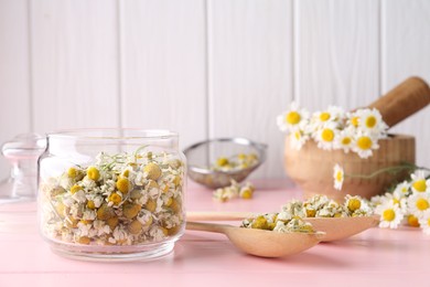 Photo of Chamomile flowers in glass jar and spoons on pink wooden table