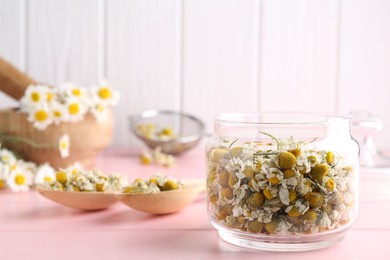 Photo of Chamomile flowers in glass jar and spoons on pink wooden table