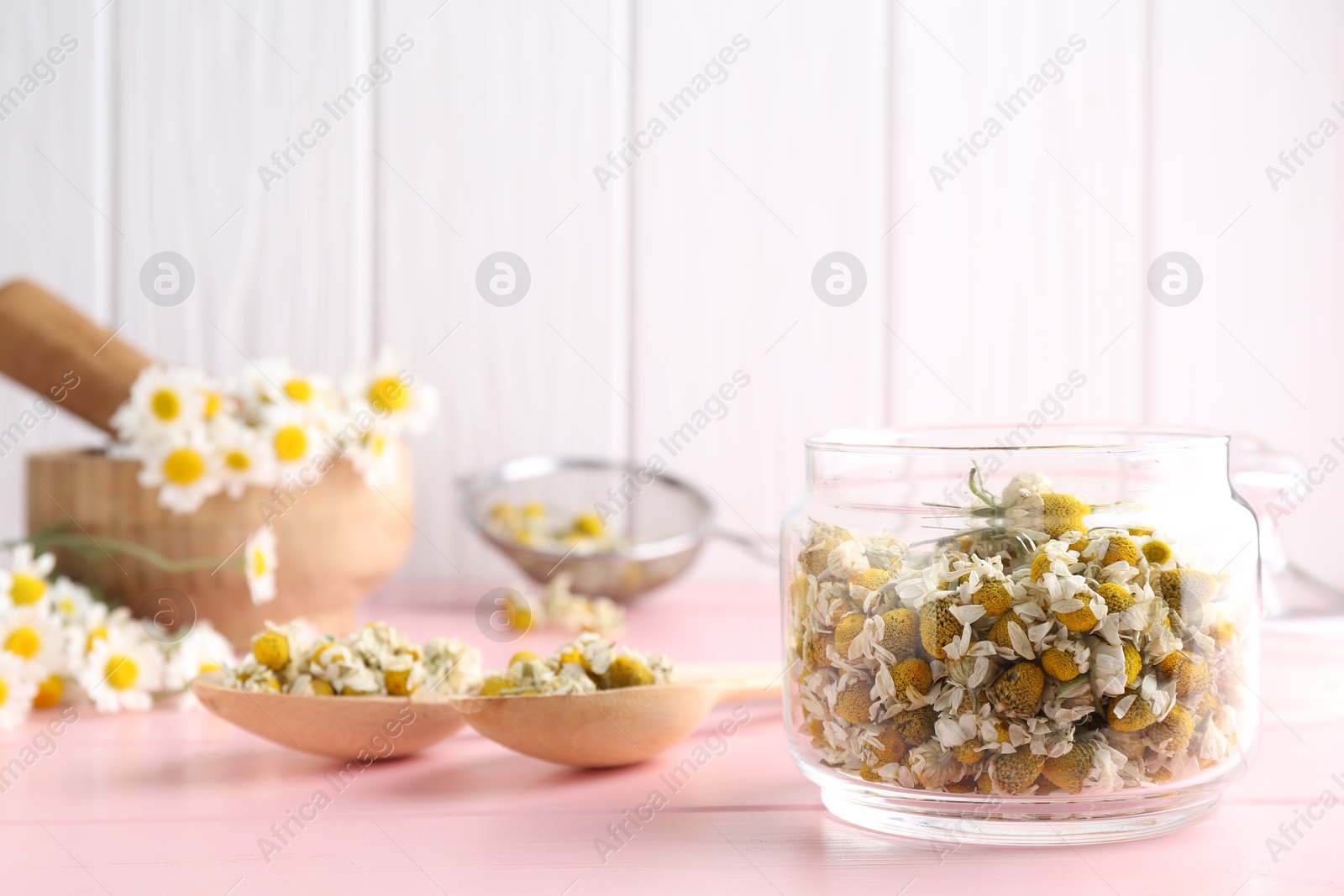 Photo of Chamomile flowers in glass jar and spoons on pink wooden table