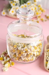 Photo of Chamomile flowers in glass jar on pink wooden table, closeup