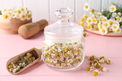 Photo of Chamomile flowers in glass jar and scoop on pink wooden table