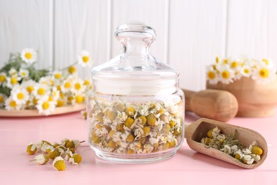 Photo of Chamomile flowers in glass jar and scoop on pink wooden table