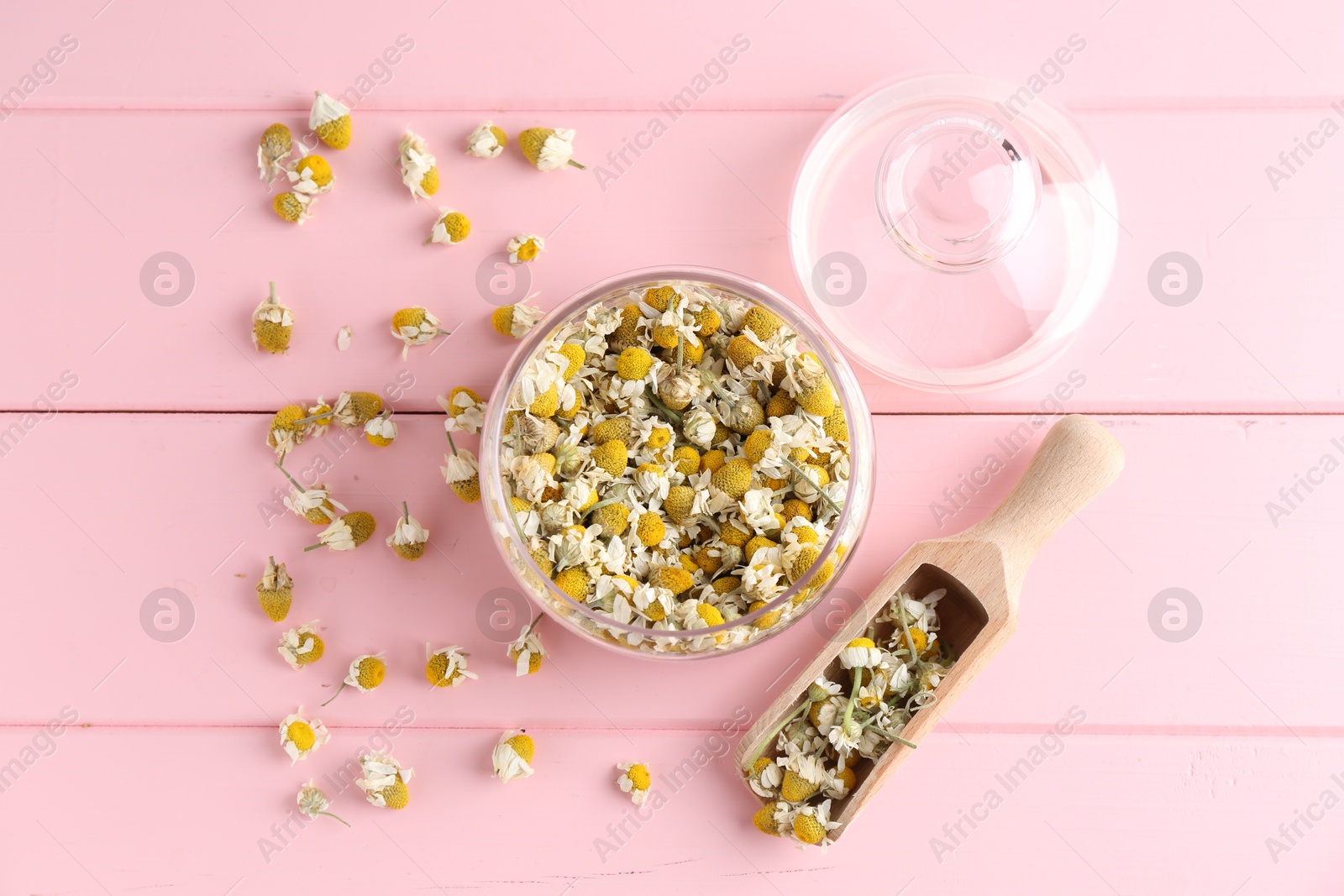 Photo of Chamomile flowers in glass jar and scoop on pink wooden table, flat lay