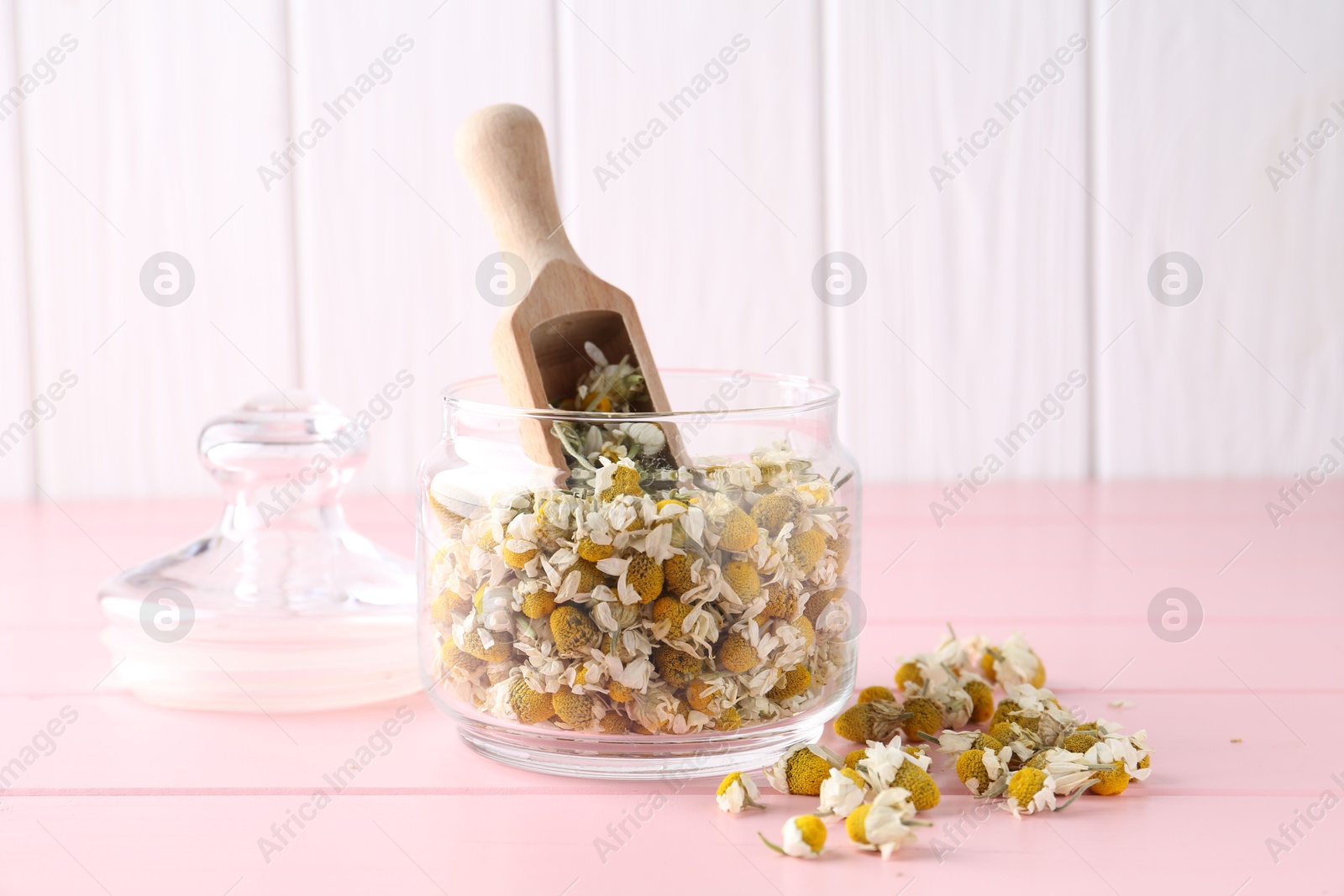 Photo of Chamomile flowers in glass jar and scoop on pink wooden table