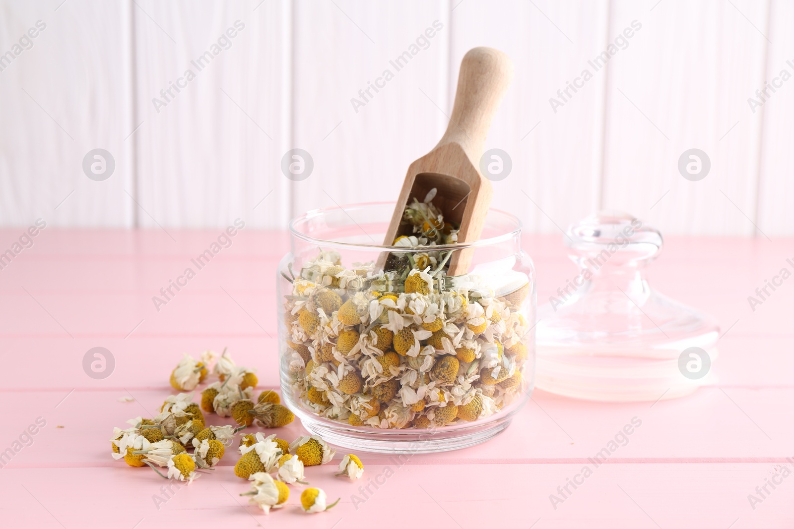 Photo of Chamomile flowers in glass jar and scoop on pink wooden table