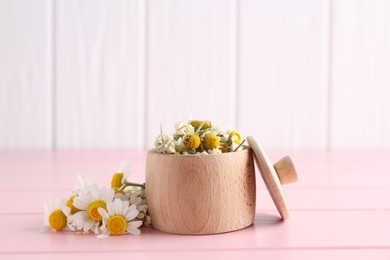 Photo of Dry and fresh chamomile flowers in bowl on pink wooden table