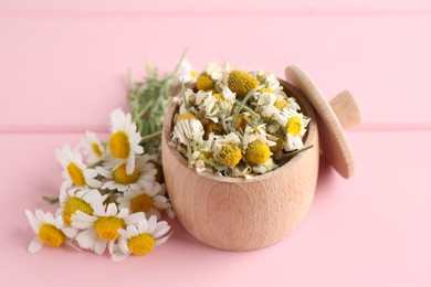 Photo of Dry and fresh chamomile flowers in bowl on pink wooden table, closeup