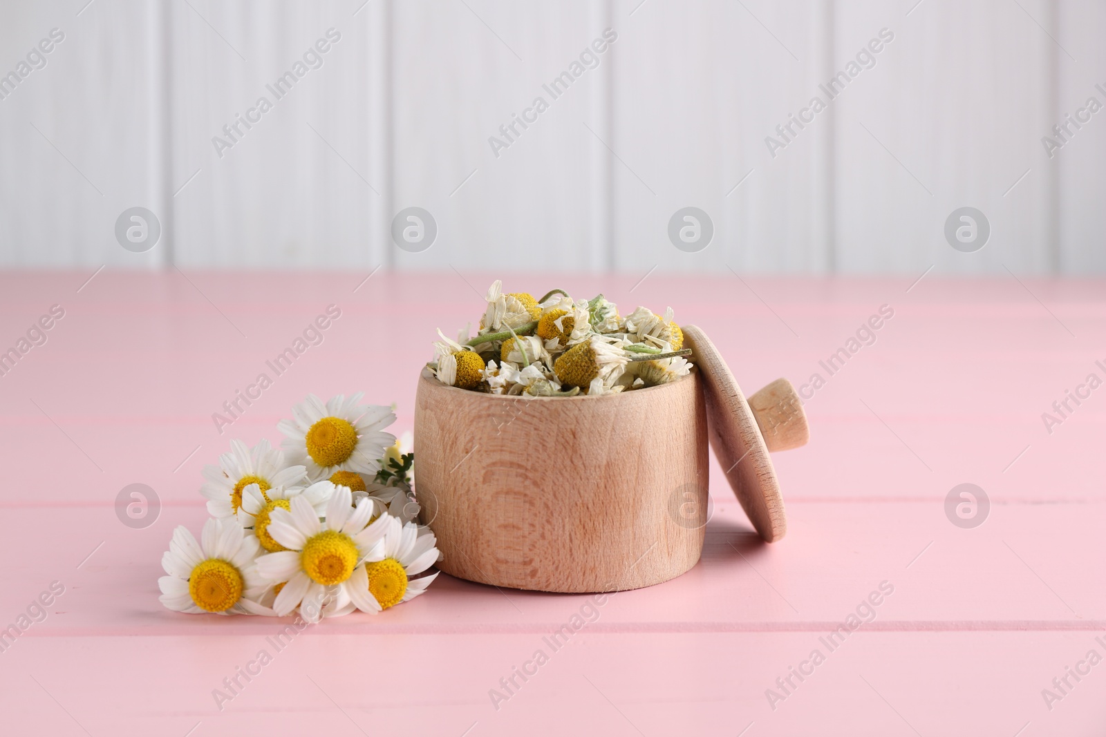 Photo of Dry and fresh chamomile flowers in bowl on pink wooden table