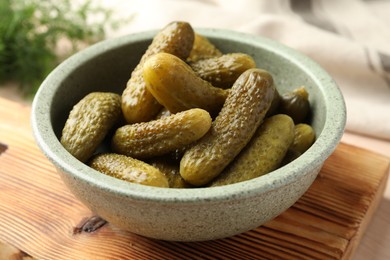 Photo of Pickled cucumbers in bowl on wooden board, closeup