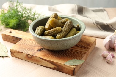 Photo of Pickled cucumbers in bowl, bay leaves and garlic on wooden table