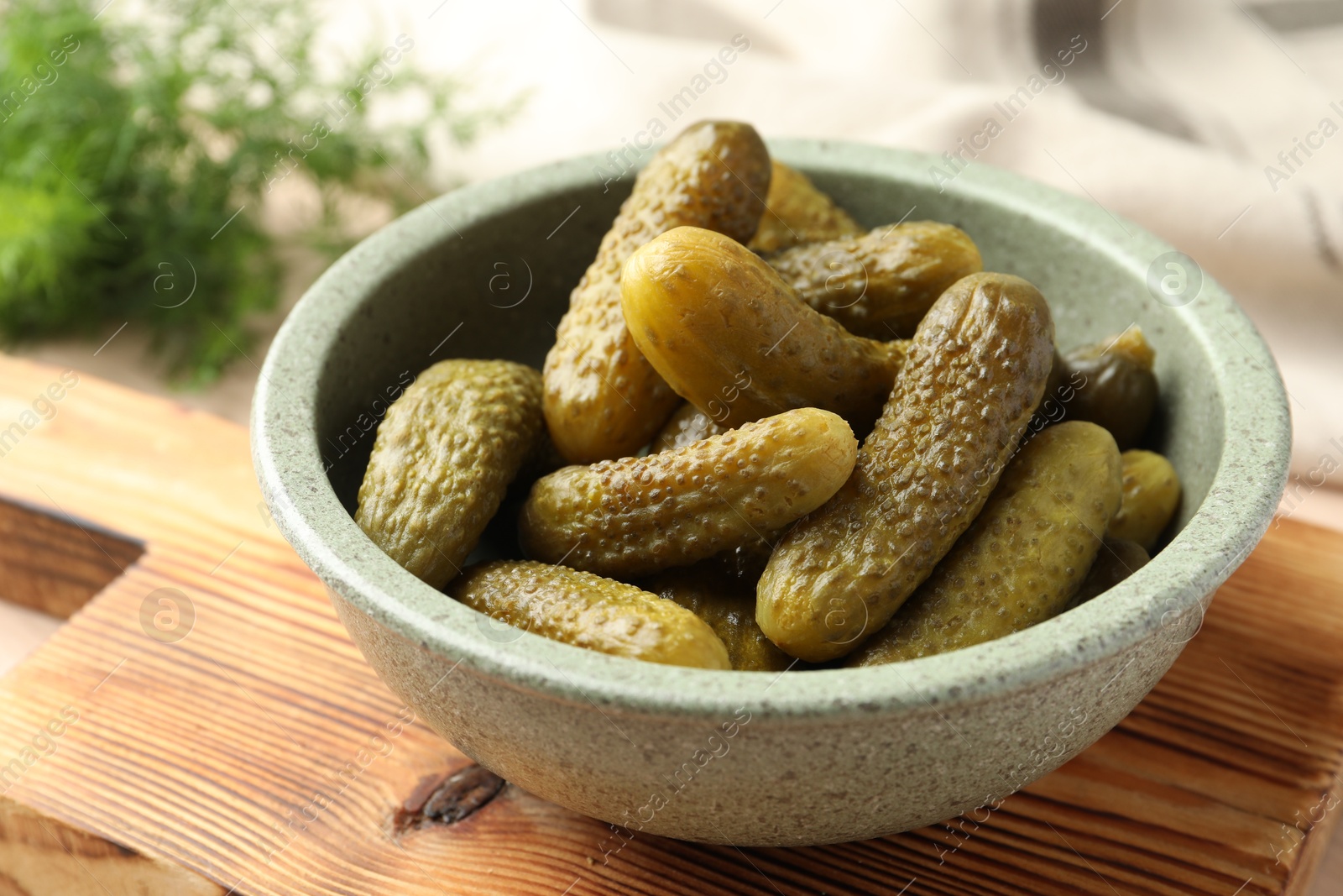 Photo of Pickled cucumbers in bowl on wooden board, closeup