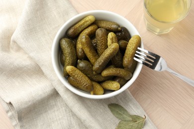 Photo of Pickled cucumbers in bowl, fork and brine on wooden table, flat lay