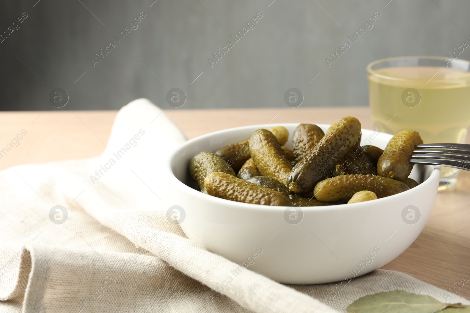 Photo of Pickled cucumbers in bowl, fork and brine on wooden table, closeup