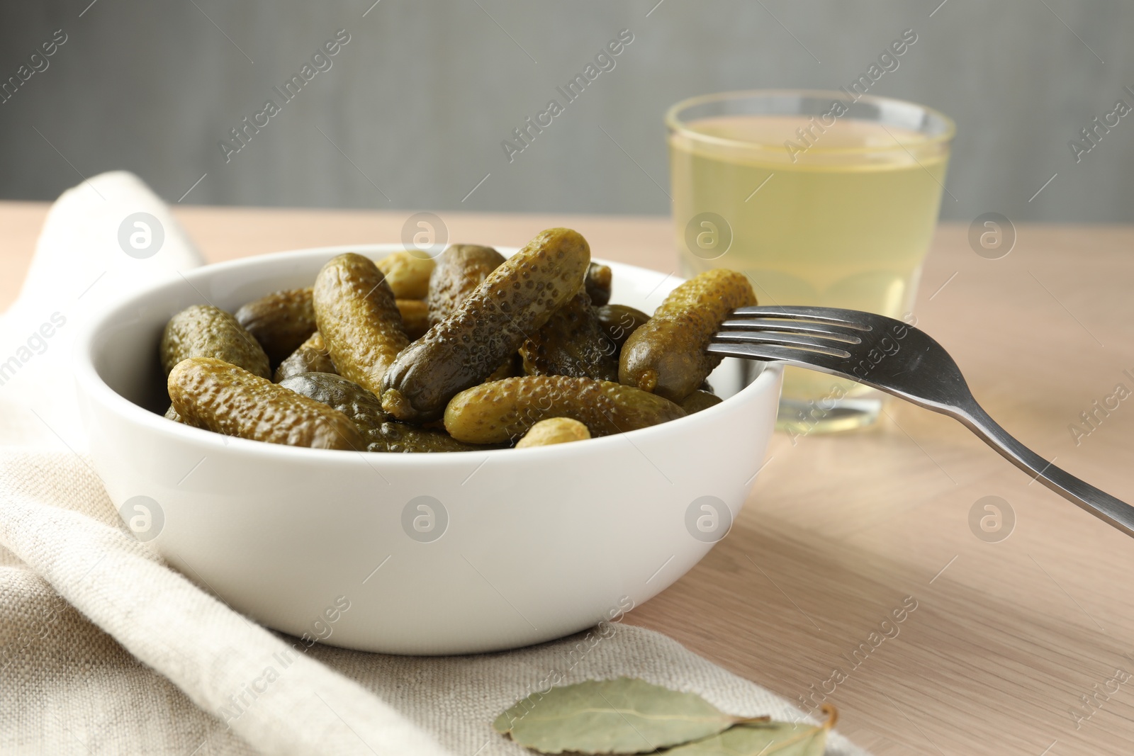 Photo of Pickled cucumbers in bowl, fork and brine on wooden table, closeup