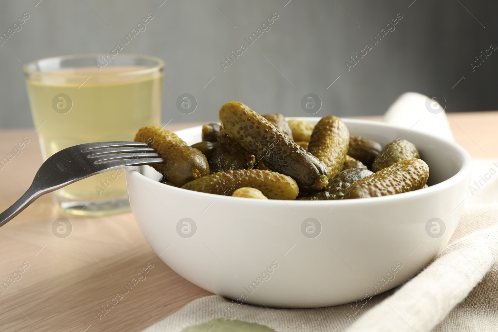 Photo of Pickled cucumbers in bowl, fork and brine on wooden table, closeup