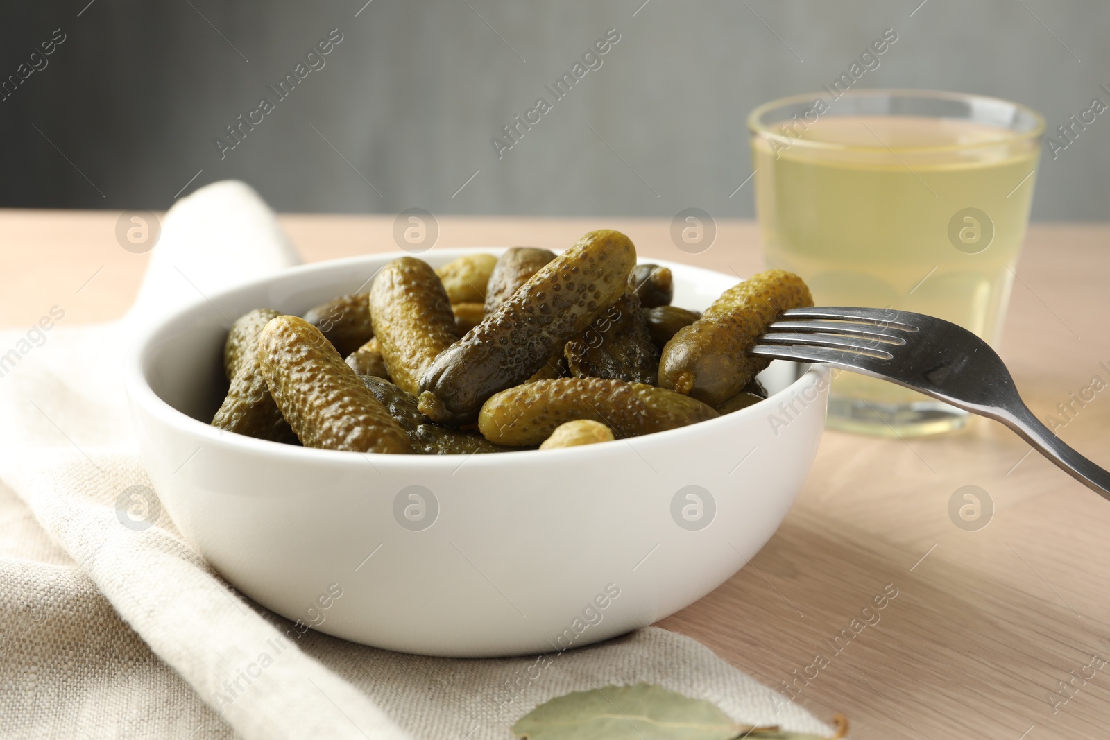 Photo of Pickled cucumbers in bowl, fork and brine on wooden table, closeup