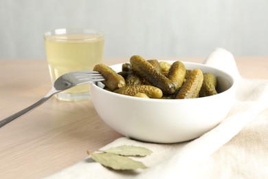 Photo of Pickled cucumbers in bowl, fork and brine on wooden table, closeup