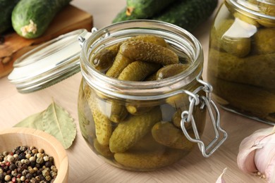 Pickled cucumbers in open jar, peppercorns and garlic on wooden table, closeup