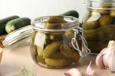 Photo of Pickled cucumbers in open jar and garlic on wooden table, closeup