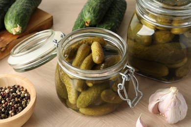Pickled cucumbers in jars, peppercorns and garlic on wooden table, closeup