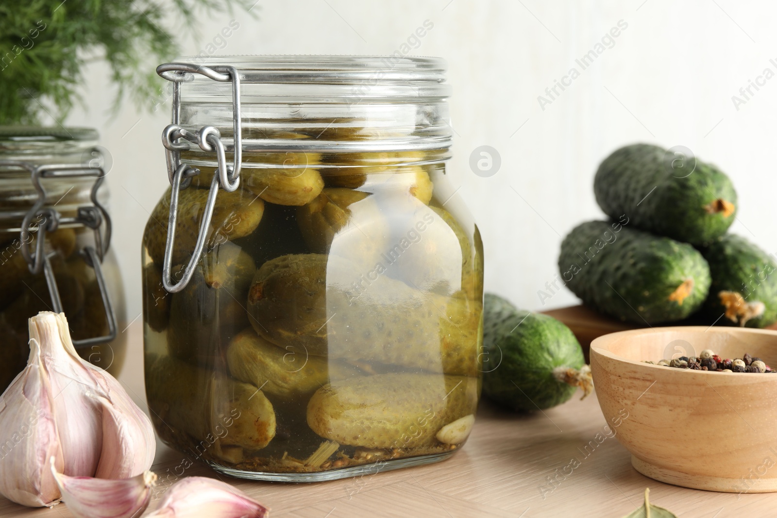 Photo of Pickled cucumbers in jars, peppercorns and garlic on wooden table, closeup